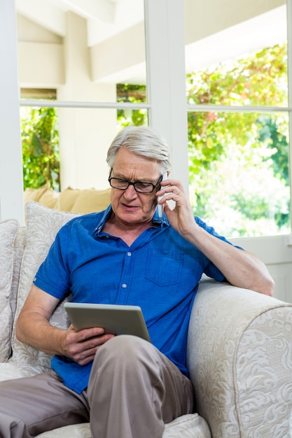 Senior hombre usando un teléfono móvil con tableta digital en casa