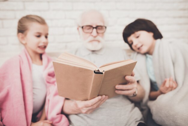 Senior Man Reading Story Book para dos nietos