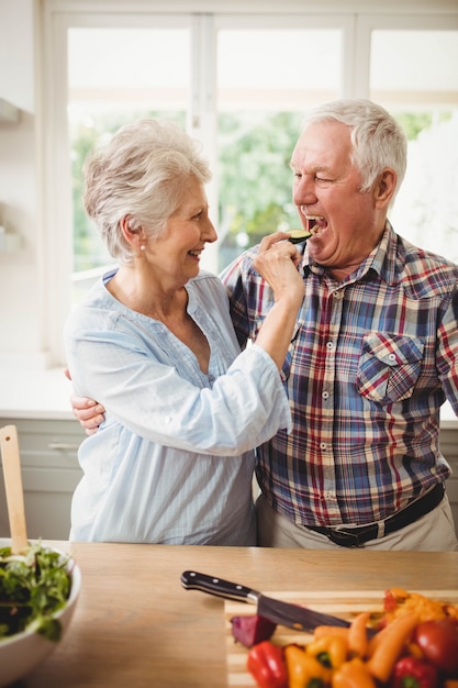 Senior mujer alimentando una rodaja de pepino al hombre senior
