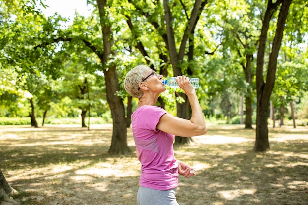 Senior mujer caucásica tomando un descanso y bebiendo agua después de un largo entrenamiento en la naturaleza.