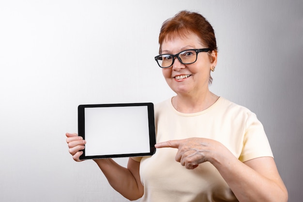 Senior mujer con gafas muestra una tableta en blanco con una camiseta ligera