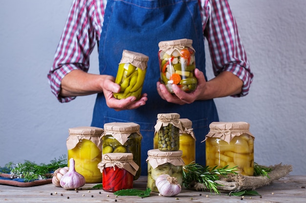 Senior mujer madura sosteniendo en las manos el frasco con conservas caseras y alimentos fermentados. Variedad de verduras en escabeche y adobadas. Limpieza, economía doméstica, preservación de la cosecha