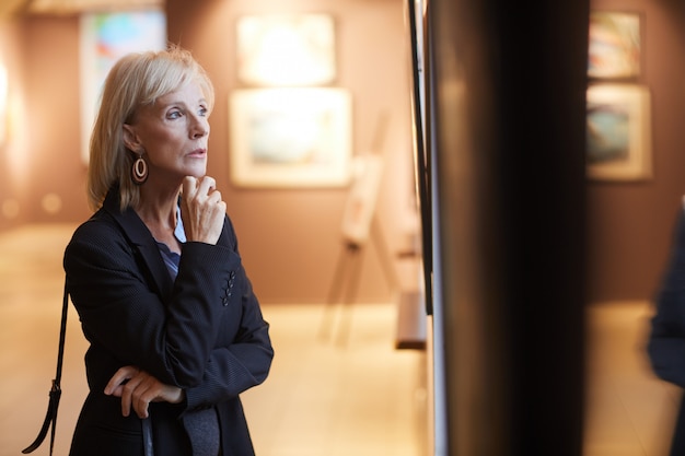 Senior mujer mirando pinturas en la galería de arte