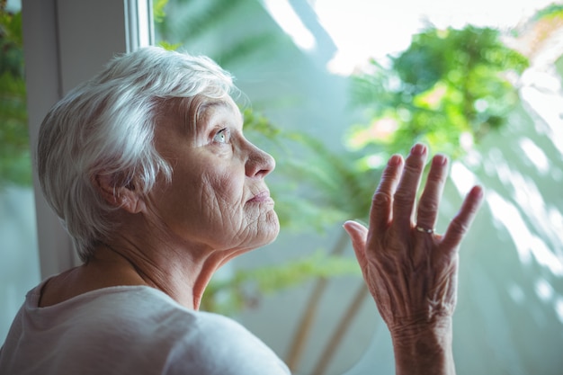 Senior mujer mirando por la ventana de la casa