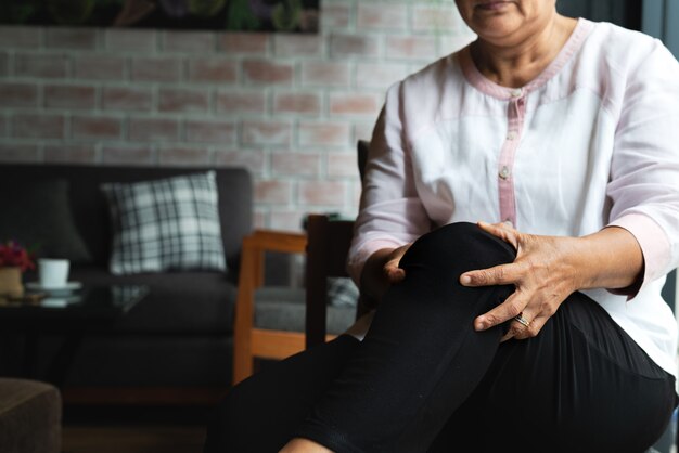 Senior mujer que sufre de dolor de rodilla en casa, problema de salud