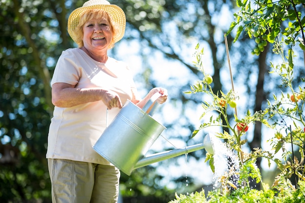 Senior mujer regando las plantas con regadera en jardín