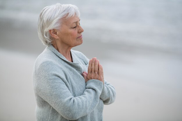 Senior mujer rezando en la playa