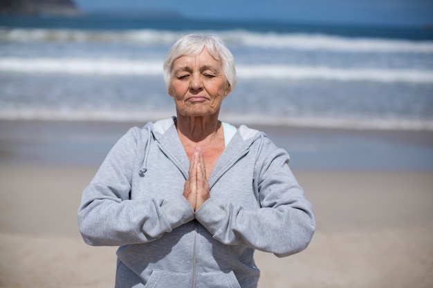 Senior mujer rezando en la playa