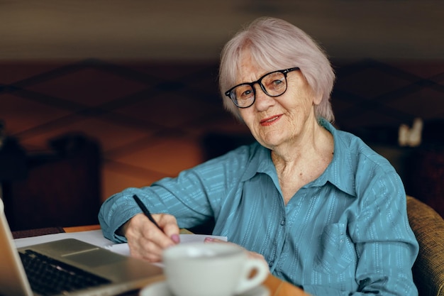 Senior mujer sentada en un café con una taza de café y una computadora portátil Freelancer funciona sin cambios