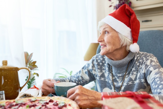 Senior mujer con sombrero de santa en la mesa de la cena