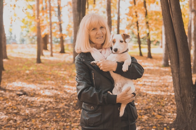 Senior mujer sonriente abrazando a su perro en el parque de otoño. El envejecimiento activo y el concepto de mascotas.