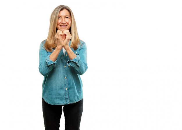 sênior mulher bonita sorrindo, olhando feliz e apaixonada, fazendo a forma de um coração com as mãos. F