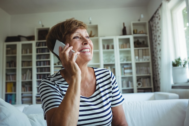 Sênior mulher falando no celular na sala de estar