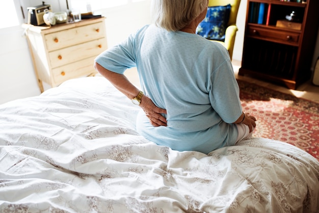 Sênior mulher sentada na cama com dor