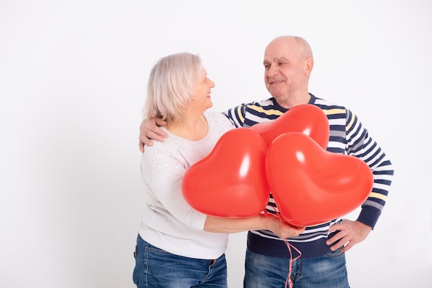 Senior pareja abrazándose sosteniendo globos de corazón rojo.