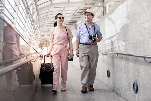 Senior pareja asiática con una mujer arrastrando una maleta y hablando alegremente con una sonrisa en el aeropuerto para prepararse para viajar. La felicidad de los tíos y tías en viajar viajan juntos con una sonrisa.
