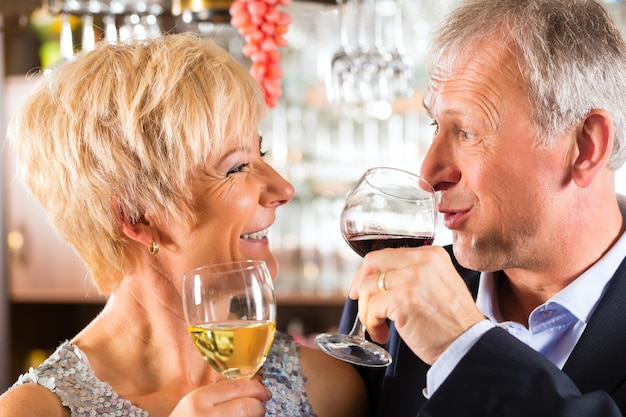 Senior pareja en el bar con una copa de vino en la mano