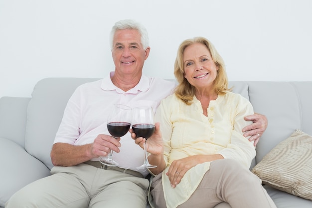 Senior pareja brindando copas de vino en casa