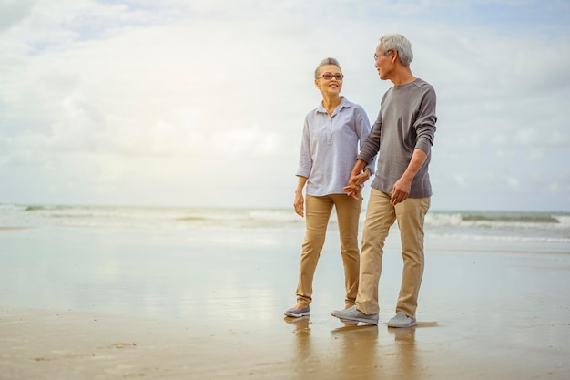 Senior pareja caminando por la playa tomados de la mano al amanecer, planificar un seguro de vida en el concepto de jubilación.