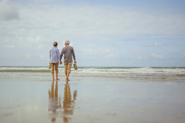 Senior pareja caminando por la playa tomados de la mano al amanecer, planificar un seguro de vida en el concepto de jubilación.