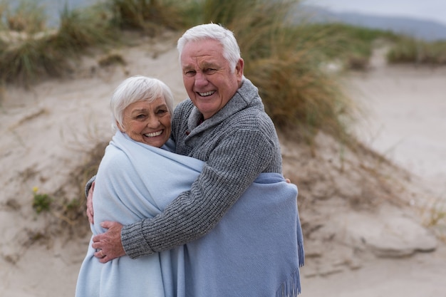 Senior pareja envuelta en un chal en la playa