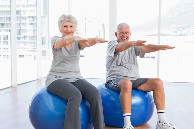 Senior pareja haciendo ejercicios de estiramiento en bolas de fitness