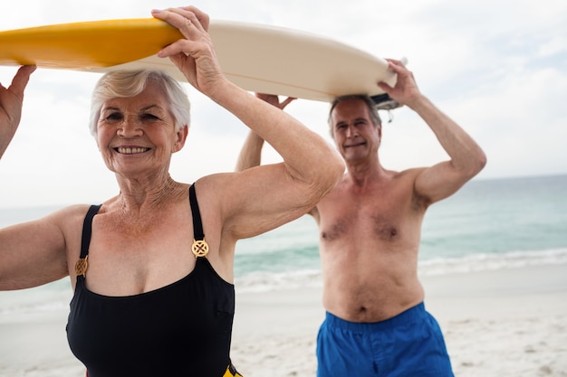 Senior pareja llevando una tabla de surf sobre su cabeza