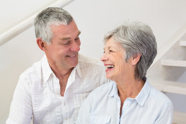 Senior pareja sentada en las escaleras sonriendo el uno al otro