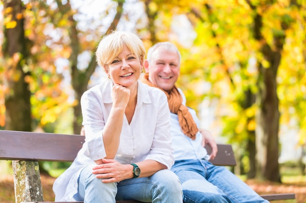 Senior pareja sentada en parte banco en otoño