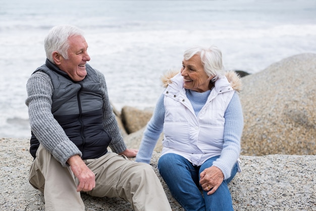 Senior pareja sentada en la roca en la playa