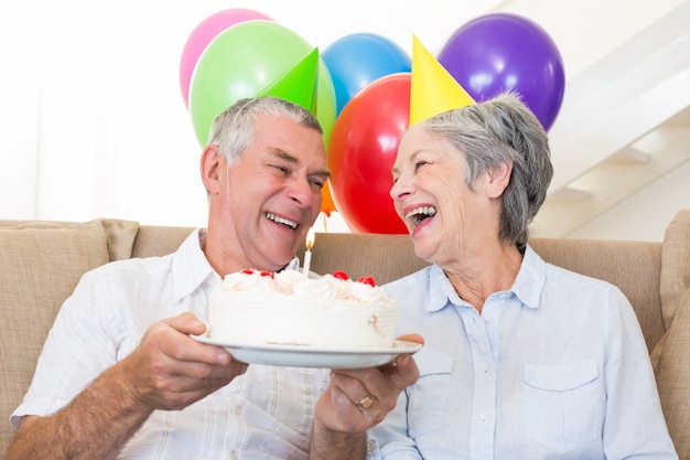 Senior pareja sentada en el sofá celebrando un cumpleaños