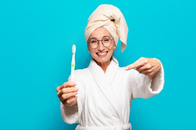 Senior Pretty Woman después de la ducha vistiendo albornoz y con un cepillo de dientes