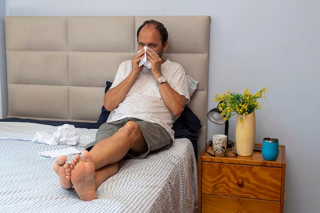 Foto sênior sentado na cama no quarto com gripe e vários papéis por causa dos espirros