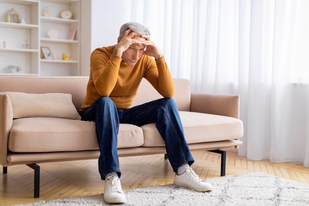 Senior sentado en el sofá con una mano en la cabeza