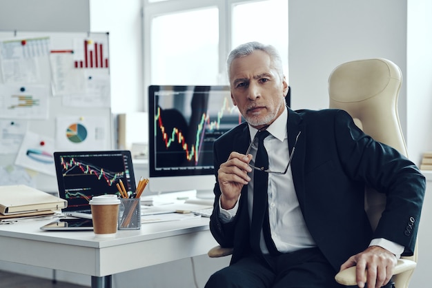 Senior Trader in eleganten Geschäften mit Blick in die Kamera während der Arbeit im Büro