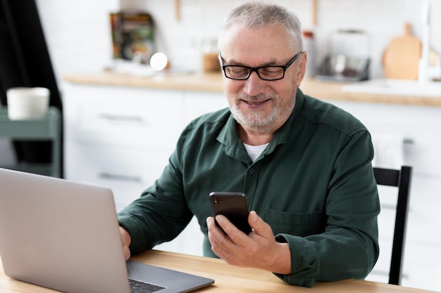 Senior woman Messaging mit Telefon am Tisch in der heimischen Küche sitzen