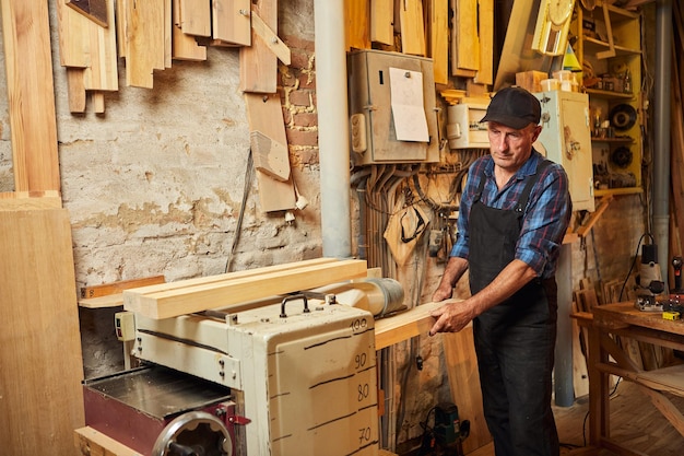 Senior Zimmermann in Uniform arbeitet mit einem Holz auf einer Holzbearbeitungsmaschine in der Tischlerei