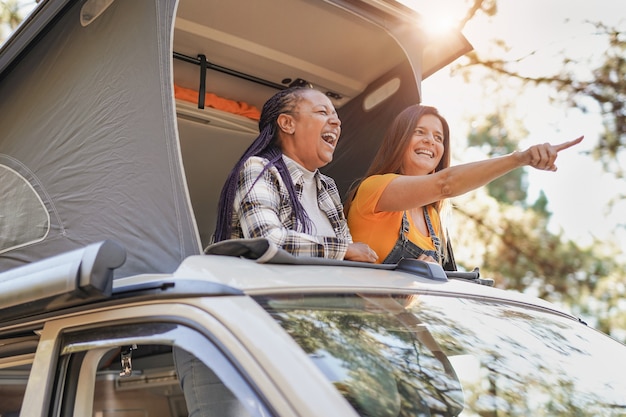 Senioren aus verschiedenen Rassen genießen Urlaub in der Natur mit Minivan - Reife Frauen auf einem Roadtrip mit Wohnmobil