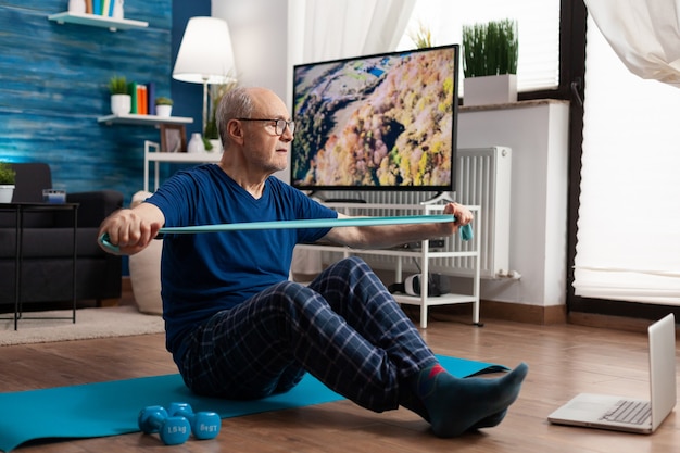 Senioren im Ruhestand sitzt auf Yogamatte mit Bein in gekreuzter Position und streckt die Armmuskulatur mit...