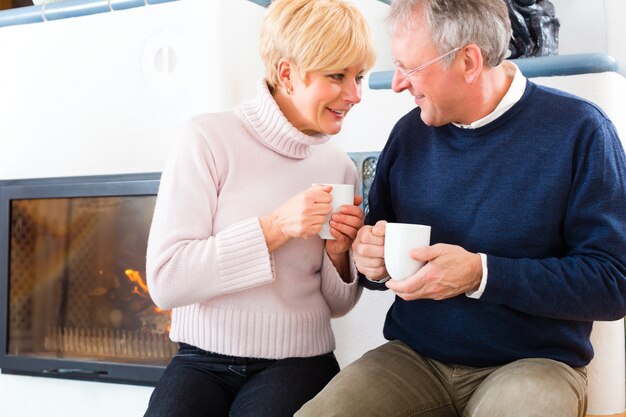 Senioren zu Hause vor dem Kamin mit Teetasse