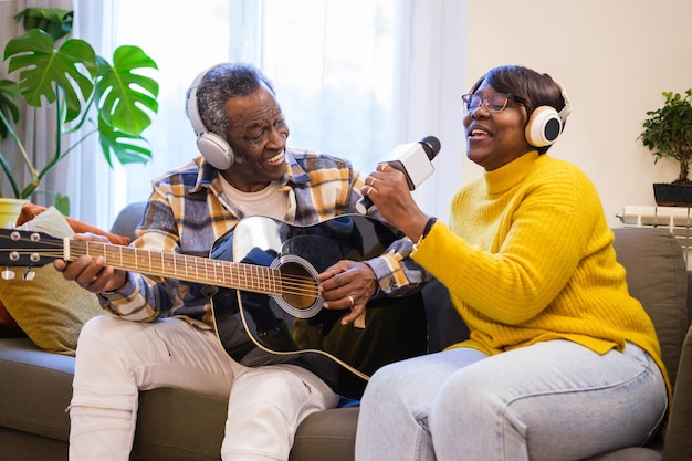 Seniorenpaar singt alte Lieder auf Stimme und Gitarre zu Hause auf dem Sofa sitzend Concept Music erinnert sich an den Ruhestand