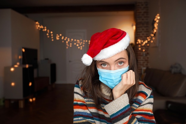 Señora aburrida en jersey de colores y sombrero rojo de Navidad se sienta en una habitación oscura con luces y tiene la cabeza en la mano en casa