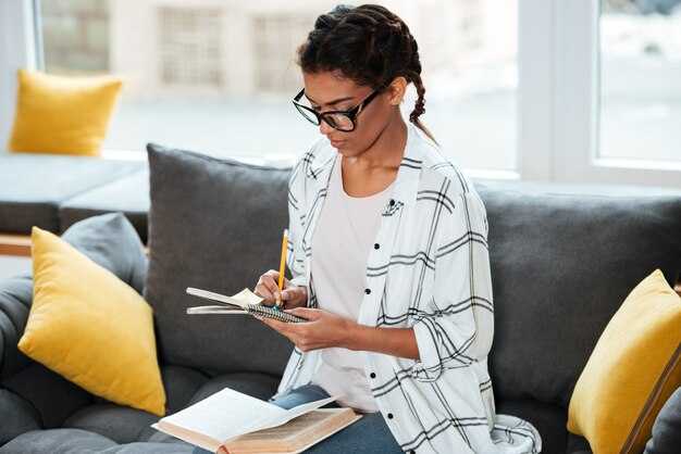 Señora africana atractiva con gafas escribiendo notas.