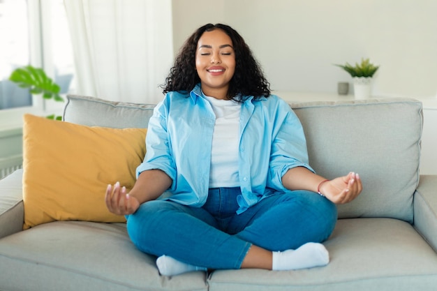 Señora afroamericana meditando con los ojos cerrados sentado en casa