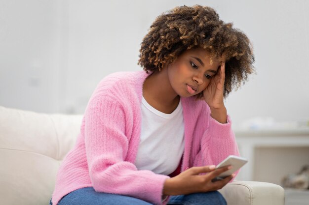 Señora afroamericana molesta usando el teléfono en casa