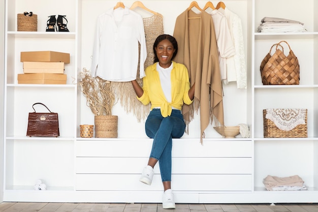 Señora afroamericana sentada en el armario entre la ropa en casa