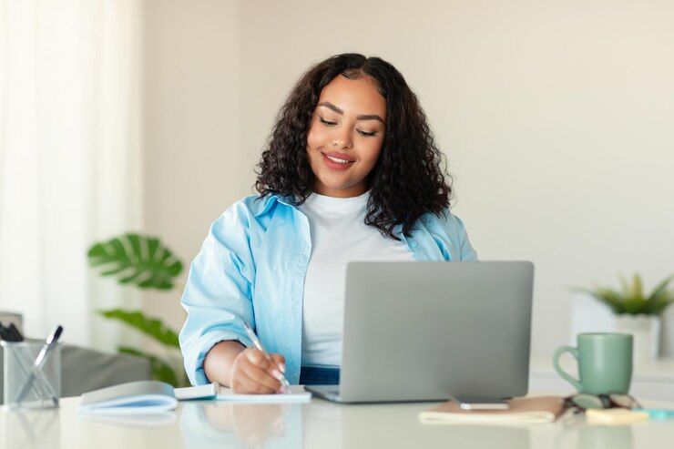 Señora afroamericana usando una computadora portátil tomando notas trabajando en la oficina