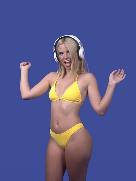 Señora alegre en auriculares y bikini cantando en estudio azul