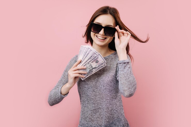 Señora alegre en gafas de sol usando billetes de dólar como ventilador