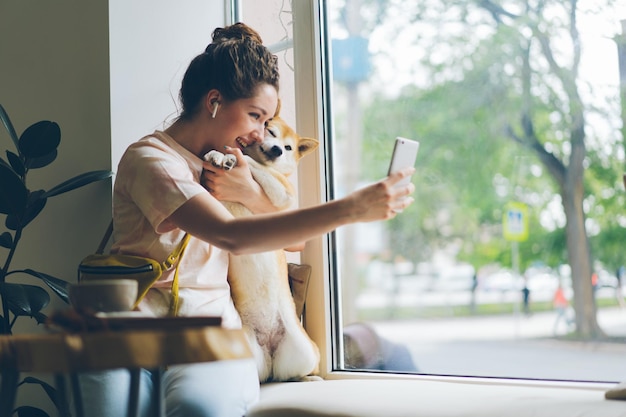 Señora alegre tomando selfie con perrito en el café usando la cámara del teléfono inteligente